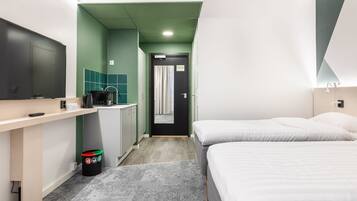 Habitación de hotel con cama, escritorio con computadora, kitchenette pequeña y baño con ducha.