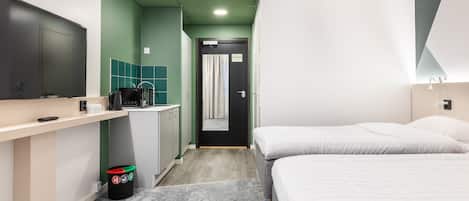 A hotel room with a bed, a desk with a computer, a small kitchenette, and a bathroom with a shower.