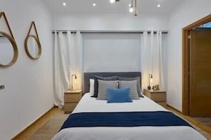 A bedroom with a bed, two bedside tables with lamps, a large mirror, and a wooden door.