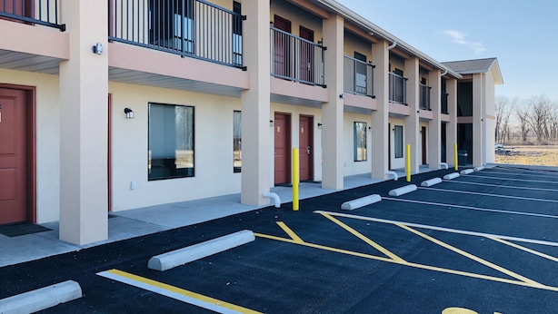 Un hôtel à plusieurs étages doté de balcons, un parking avec des places délimitées et un ciel dégagé.
