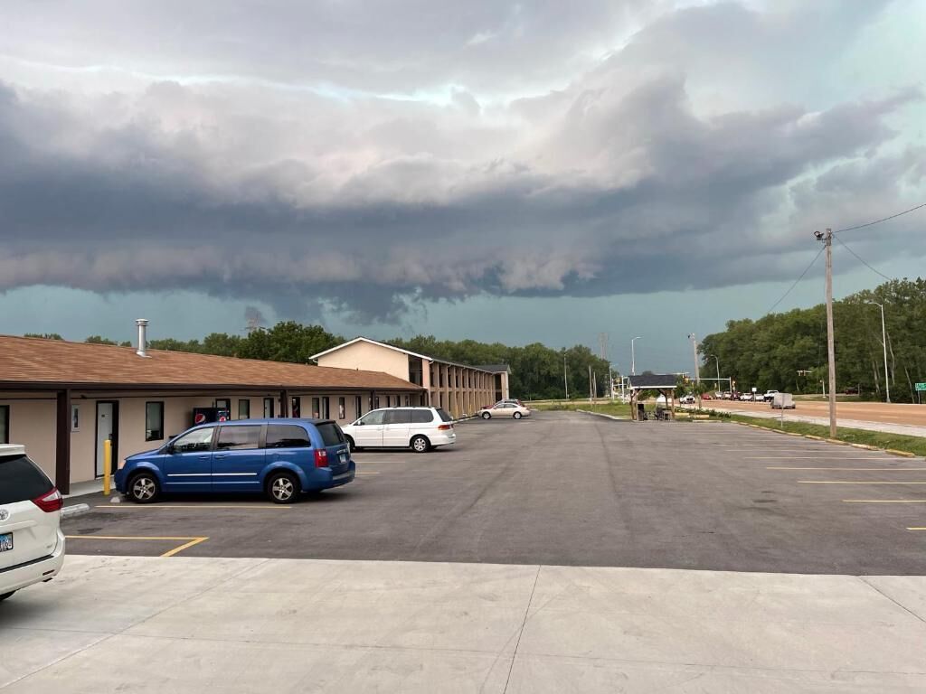 A parking lot with several cars, a building with a brown roof, and a stormy sky.