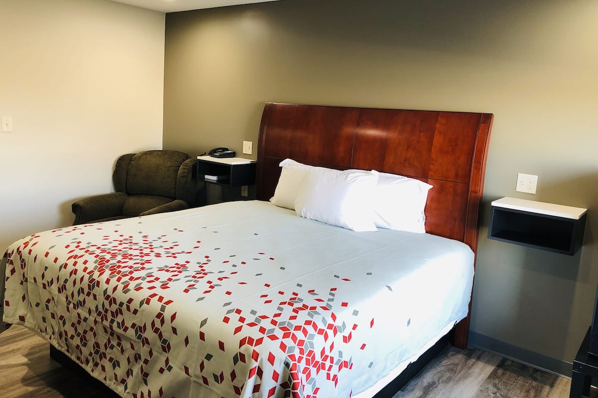Hotellihuone, jossa on suuri sänky, puinen pääty, työpöytä puhelimella, tuoli ja yöpöytä.