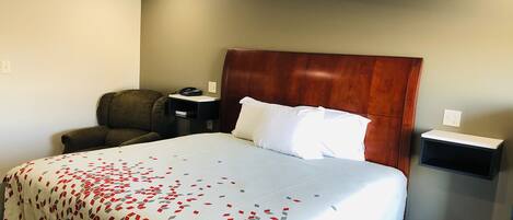 A hotel room with a large bed, a wooden headboard, a desk with a phone, a chair, and a nightstand.