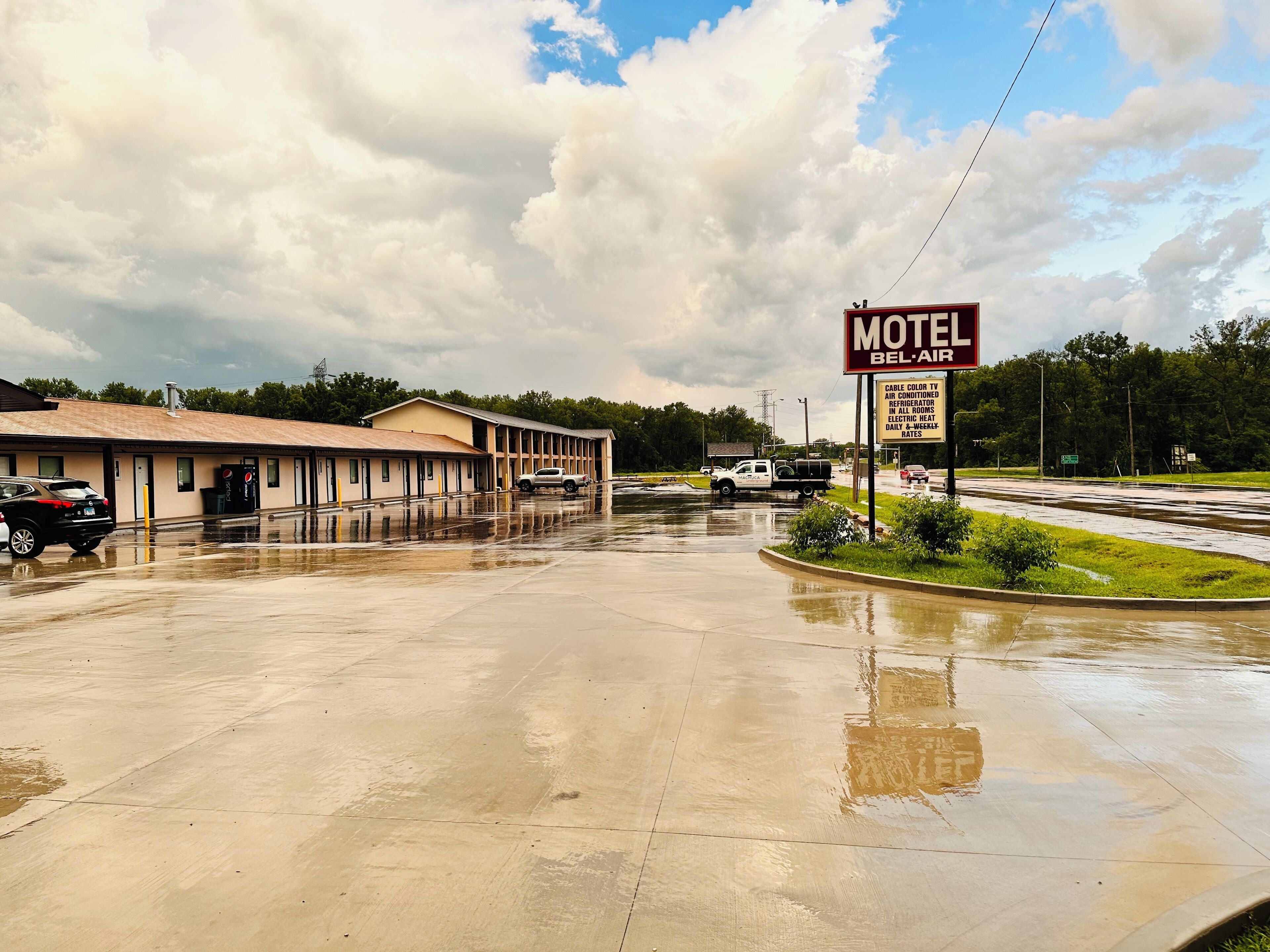 A motel with a large parking lot and a sign advertising amenities like cable TV, air conditioning, and an electric heater.
