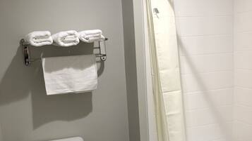 A bathroom with a toilet, a towel rack with folded towels, a trash can, and a shower area with a curtain.