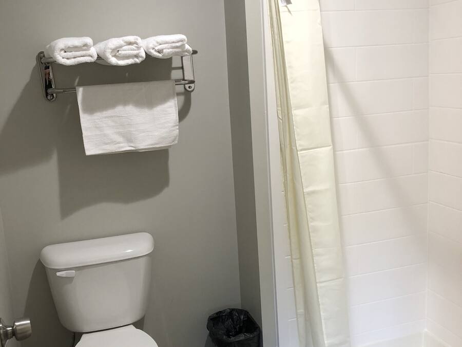 A bathroom with a toilet, a towel rack with folded towels, a trash can, and a shower area with a curtain.