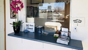 Un comptoir d’accueil avec une pancarte indiquant « Les animaux ne sont pas admis », une autre pancarte indiquant « Veuillez sonner à la porte » et une fenêtre donnant sur un parking.