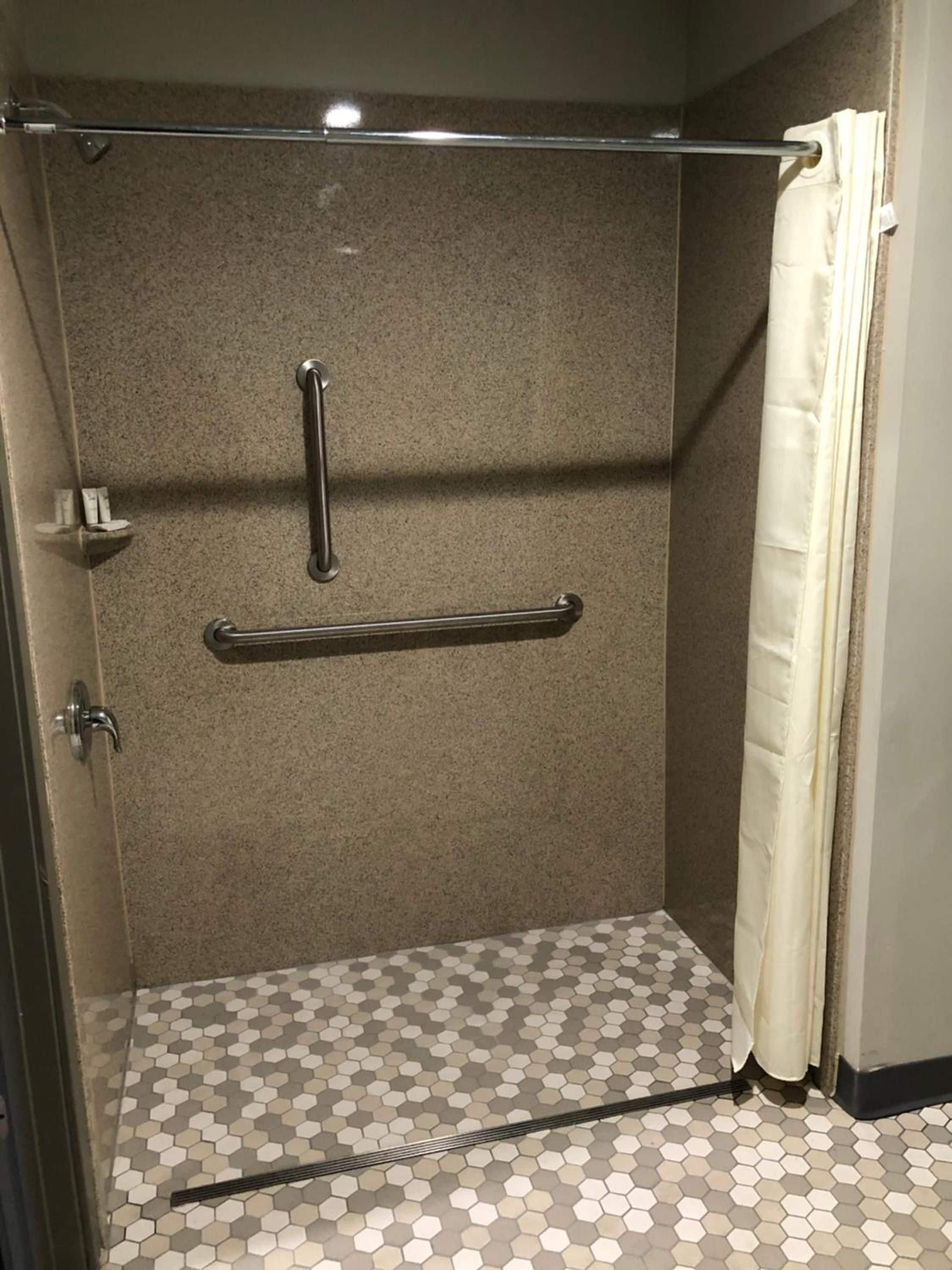 Une cabine de douche équipée d’une barre d’appui, d’un porte-serviettes et d’un sol carrelé.