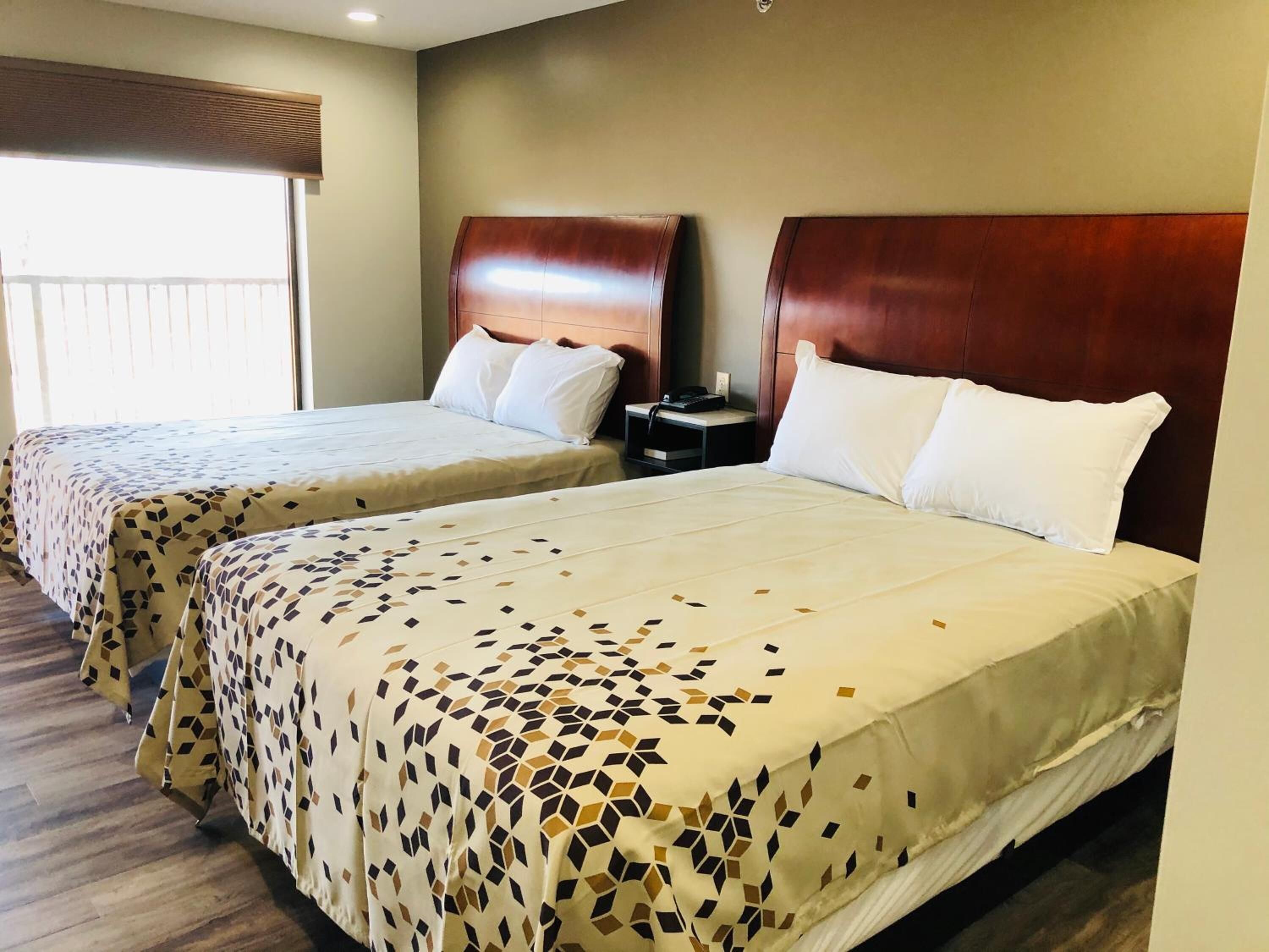Two double beds with patterned bedspreads, wooden headboards, bedside tables with lamps, and a window with blinds.