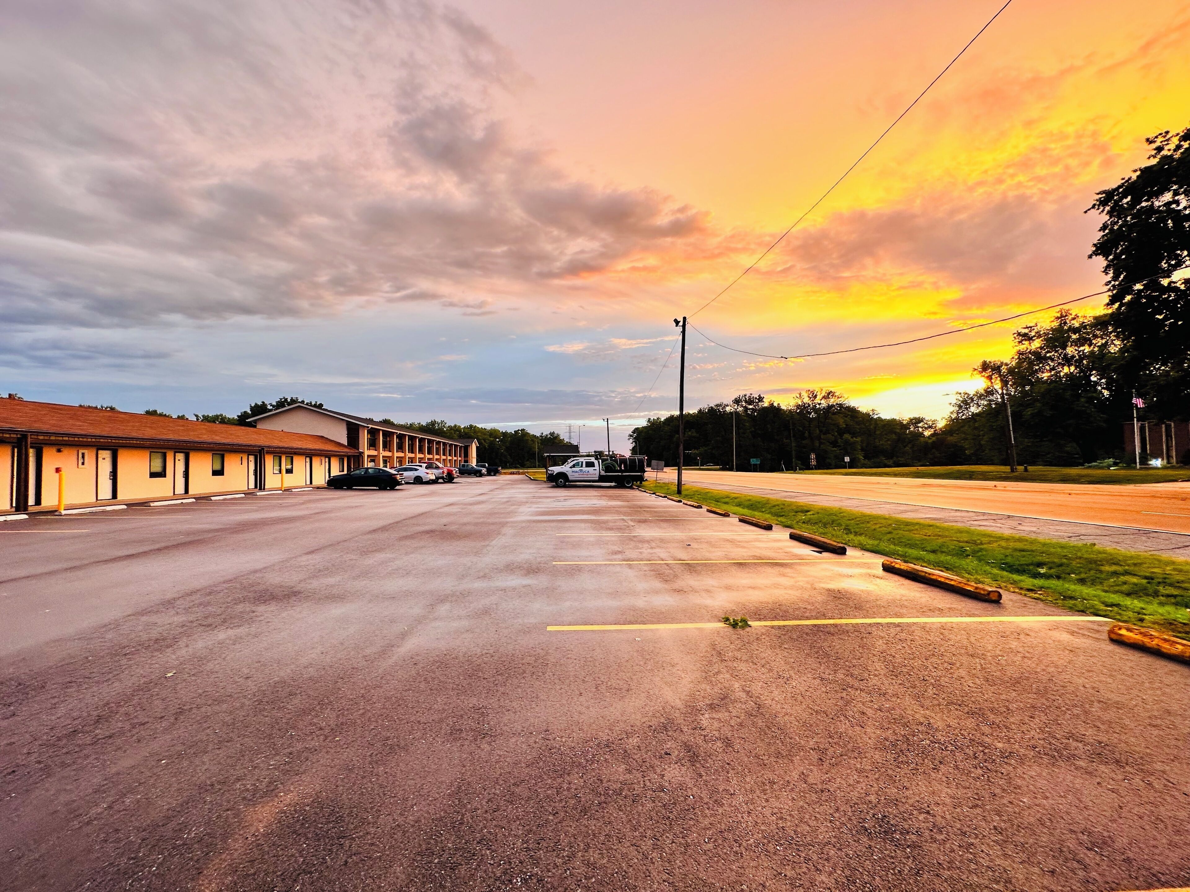 A motel with a row of rooms, a parking lot, and a road with a truck.