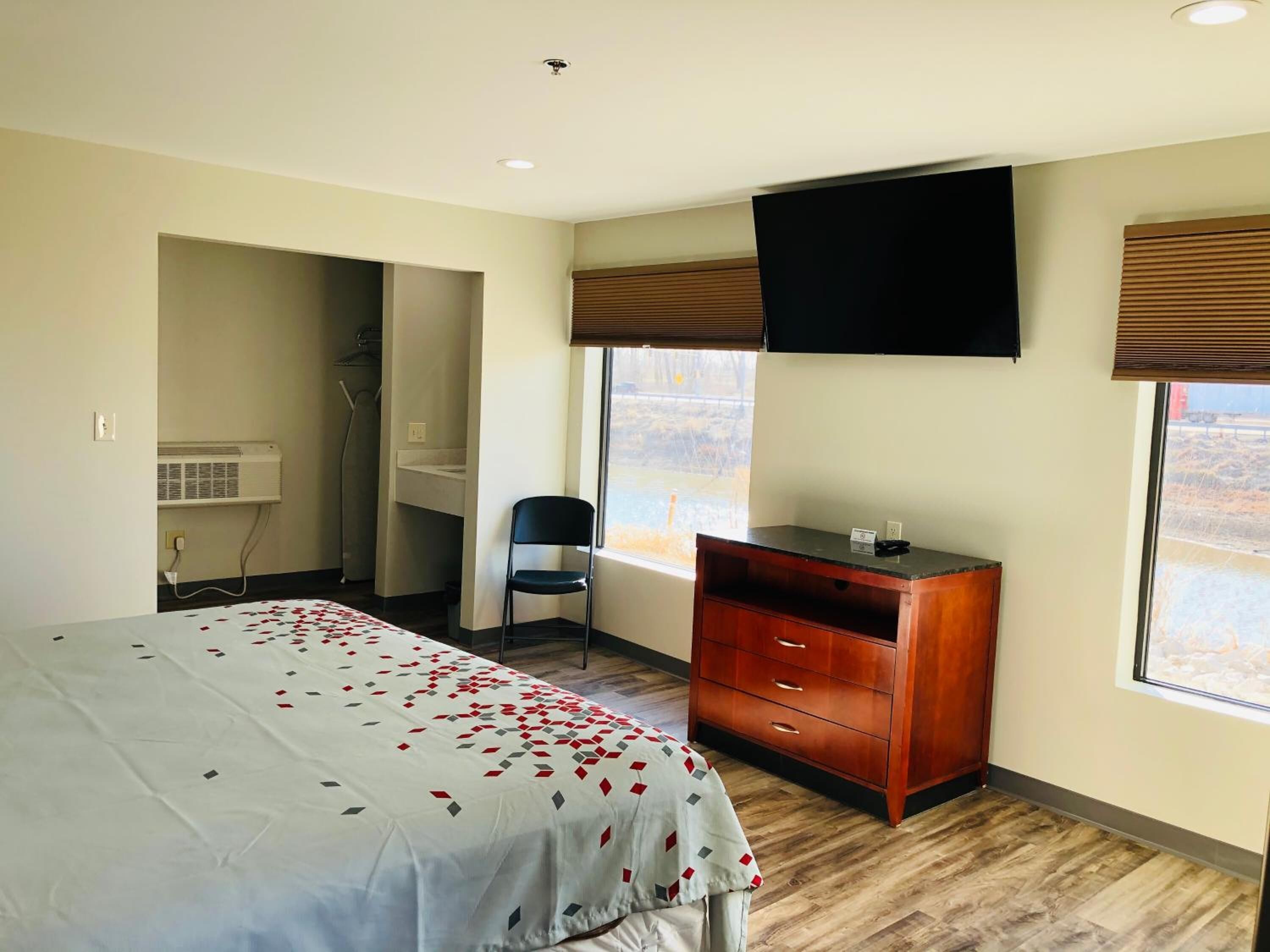 A bedroom with a bed, a desk, a chair, a TV, and a window.