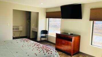 A bedroom with a bed, a desk, a chair, a TV, and a window.