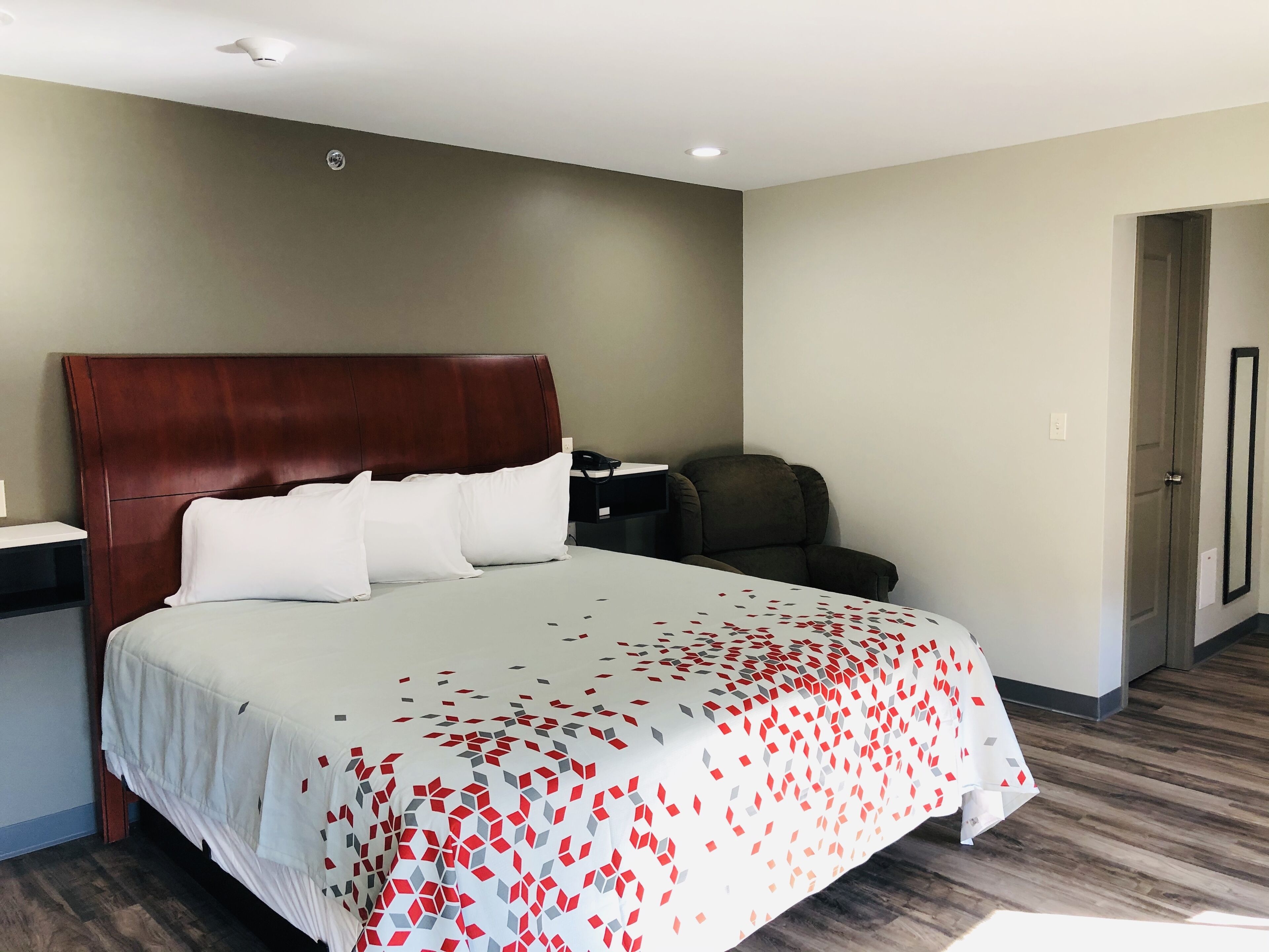Een hotelkamer met een groot bed, een bureau met telefoon, een stoel en een deur.