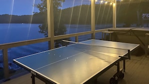 Ein Tischtennis-Tisch unter einem überdachten Bereich mit Lichterketten, mit Blick auf ein Gewässer.