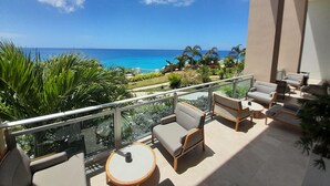 Un balcón con mobiliario exterior, vista al océano y vegetación tropical.