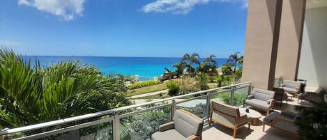 A balcony with outdoor furniture, a view of the ocean, and tropical vegetation.