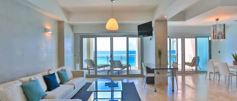 A spacious living area with a sofa, coffee table, and dining table. A large window offers a view of the ocean.