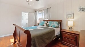A bedroom with a wooden bed, a nightstand with a lamp, a ceiling fan, and a window with curtains. - Mid-Century Vibes w/ Firepit Near UF/Downtown/Shands & Walk to Coffee Culture (Gainesville)