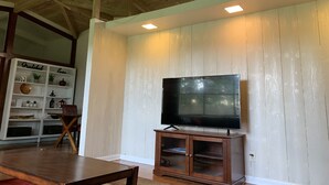 A living room with a wooden ceiling, a flat-screen TV on a wooden stand, and a shelving unit with various items. - Mid-Century Vibes w/ Firepit Near UF/Downtown/Shands & Walk to Coffee Culture (Gainesville)