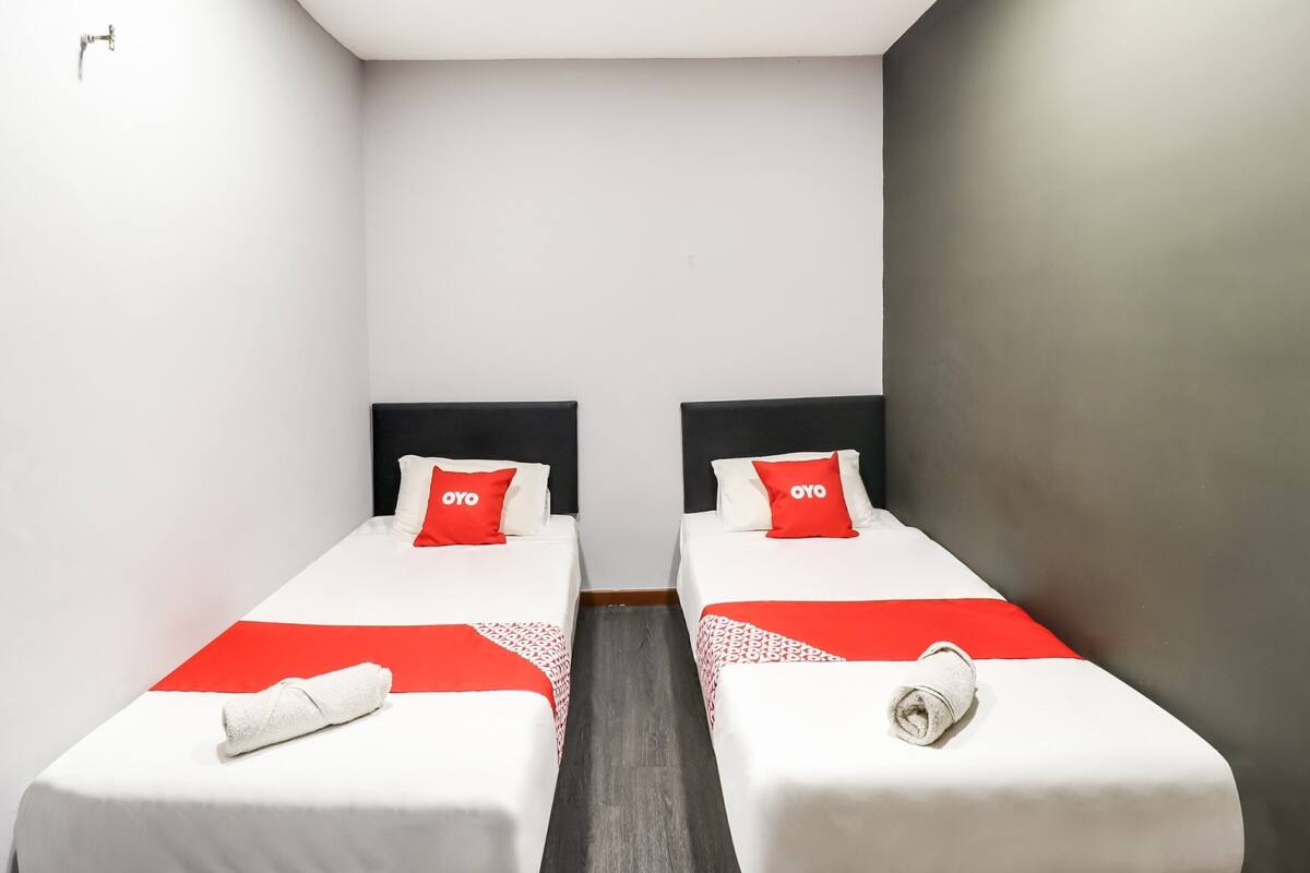 Een hotelkamer met twee enkele bedden, elk voorzien van een zwart hoofdbord, wit beddengoed en een rood kussen met 'OYO'-merk.