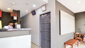 A hotel reception area with a receptionist, a grey door, a clock, and wooden furniture. - OYO 89381 Moonnight Hotel (Batu Caves)