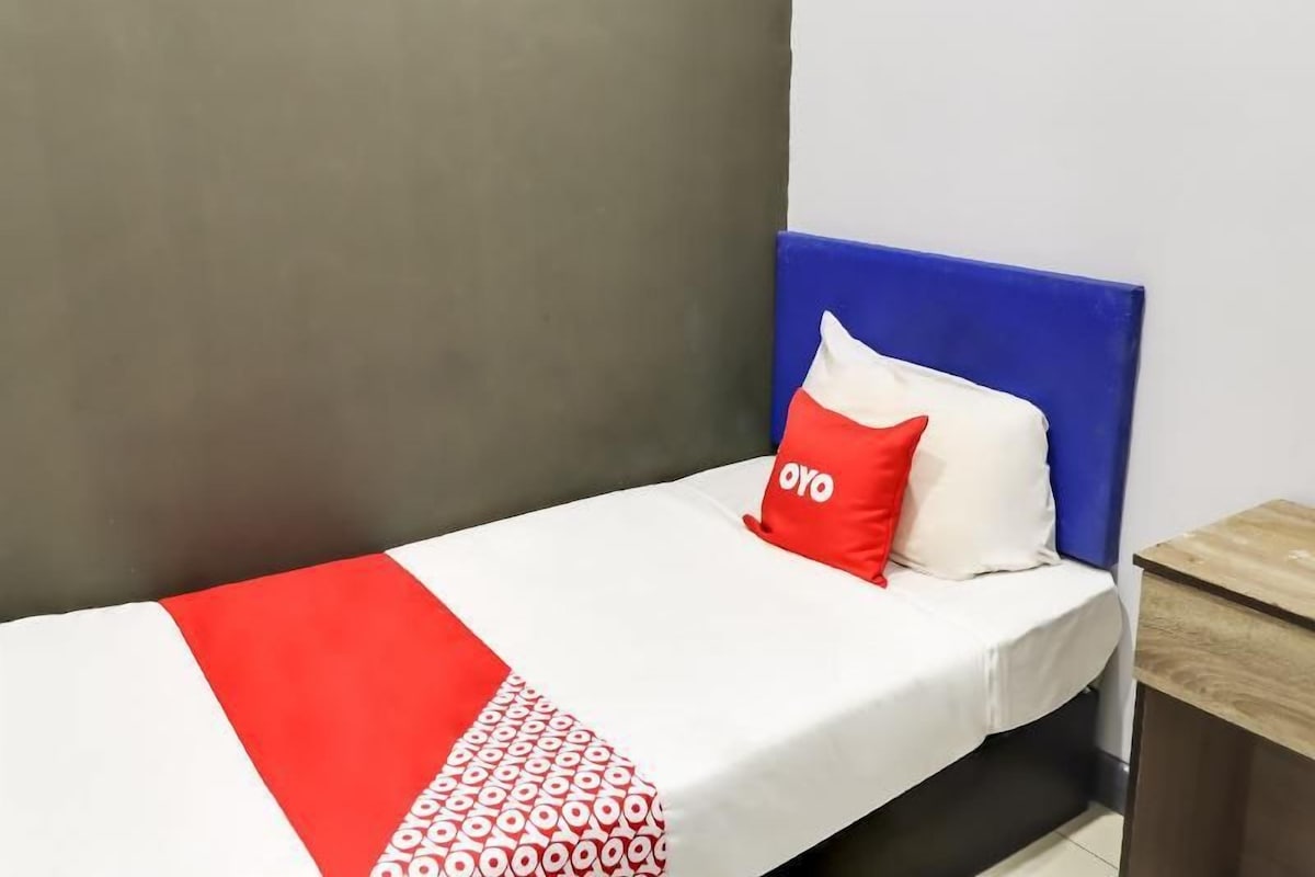A single bed with a blue headboard, a white and red bedspread, and a red pillow with 'OYO' text.
