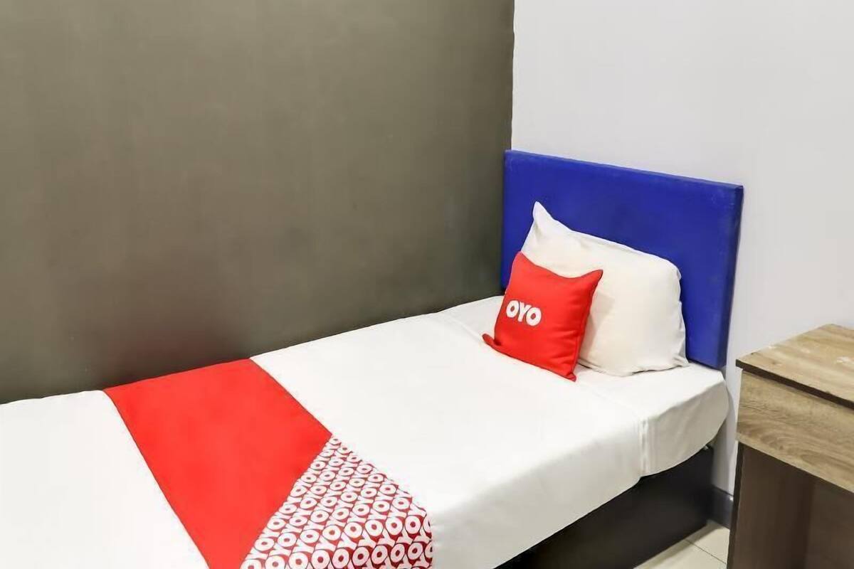 Een enkel bed met een blauw hoofdbord, een wit en rood dekbed en een rood kussen met de tekst 'OYO'.
