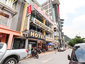 A hotel with a prominent sign, a motorcycle parked in front, and a street with cars and a blue tent. - OYO 89381 Moonnight Hotel (Batu Caves)
