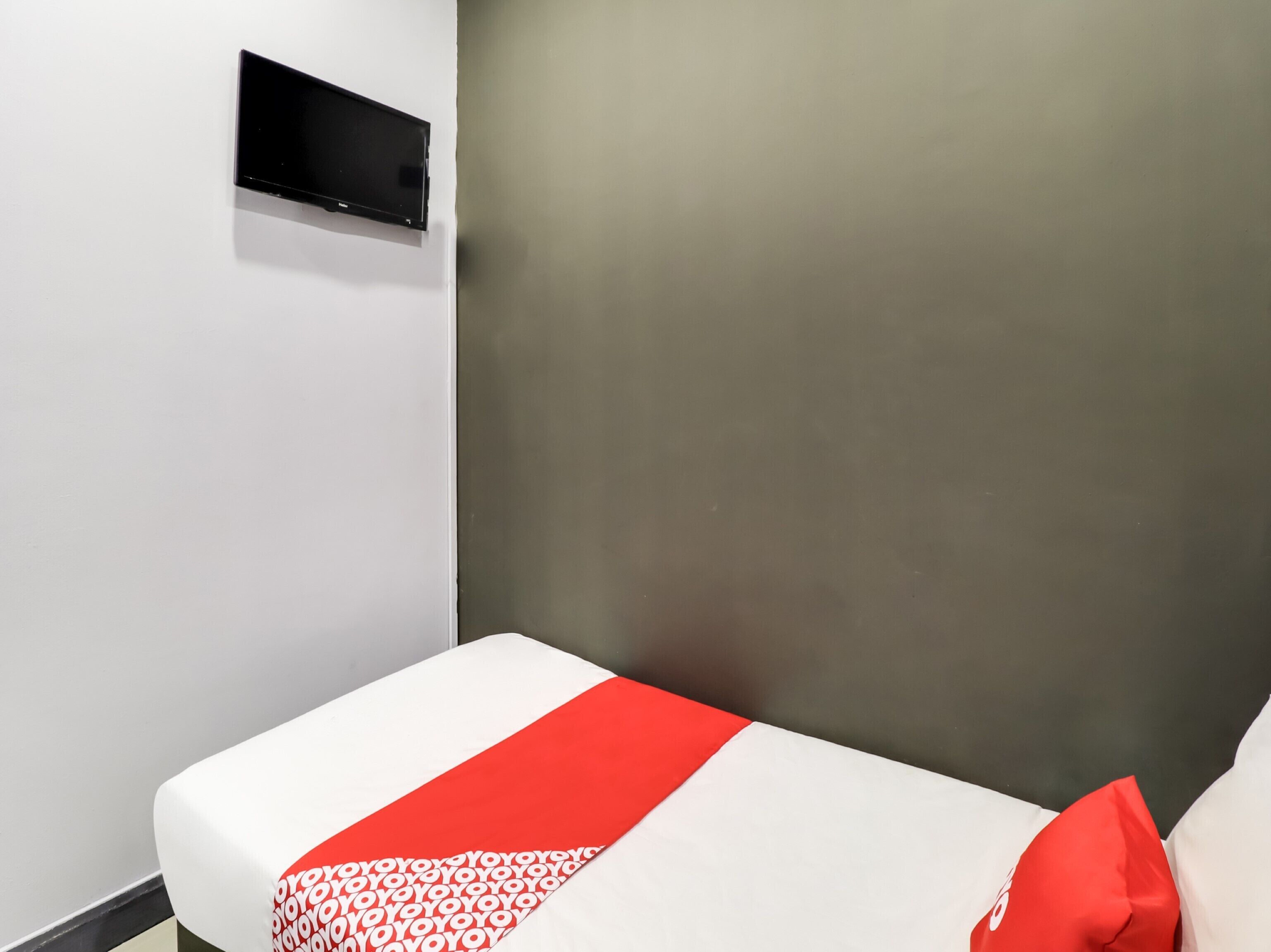 Une chambre d’hôtel avec un lit, un téléviseur à écran plat fixé au mur et une couvre-lit rouge et blanche.