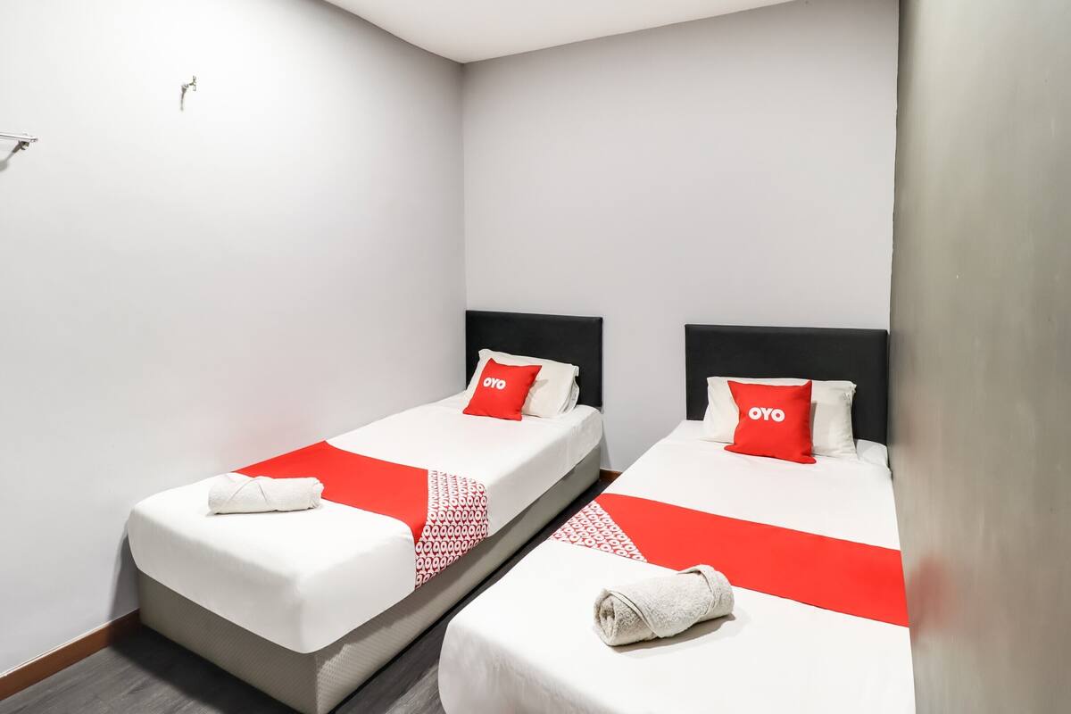 Een hotelkamer met twee eenpersoonsbedden, elk met een zwart hoofdbord, witte beddengoed en rode accenten.