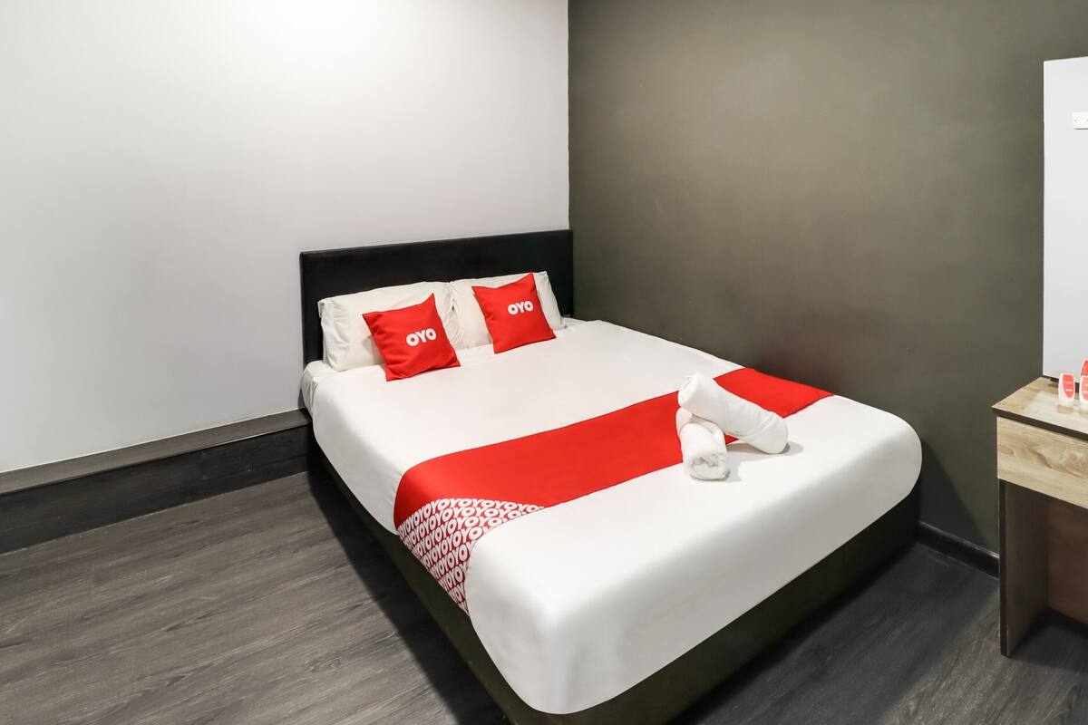 Een moderne hotelkamer met een groot bed, witte beddengoed, rode accenten en een houten nachtkastje.