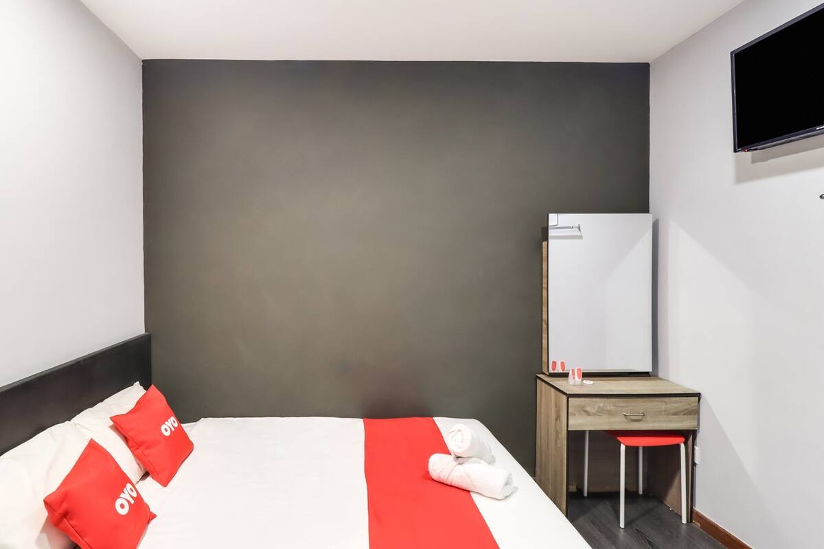 Een hotelkamer met een bed, bureau, stoel, spiegel en televisie.