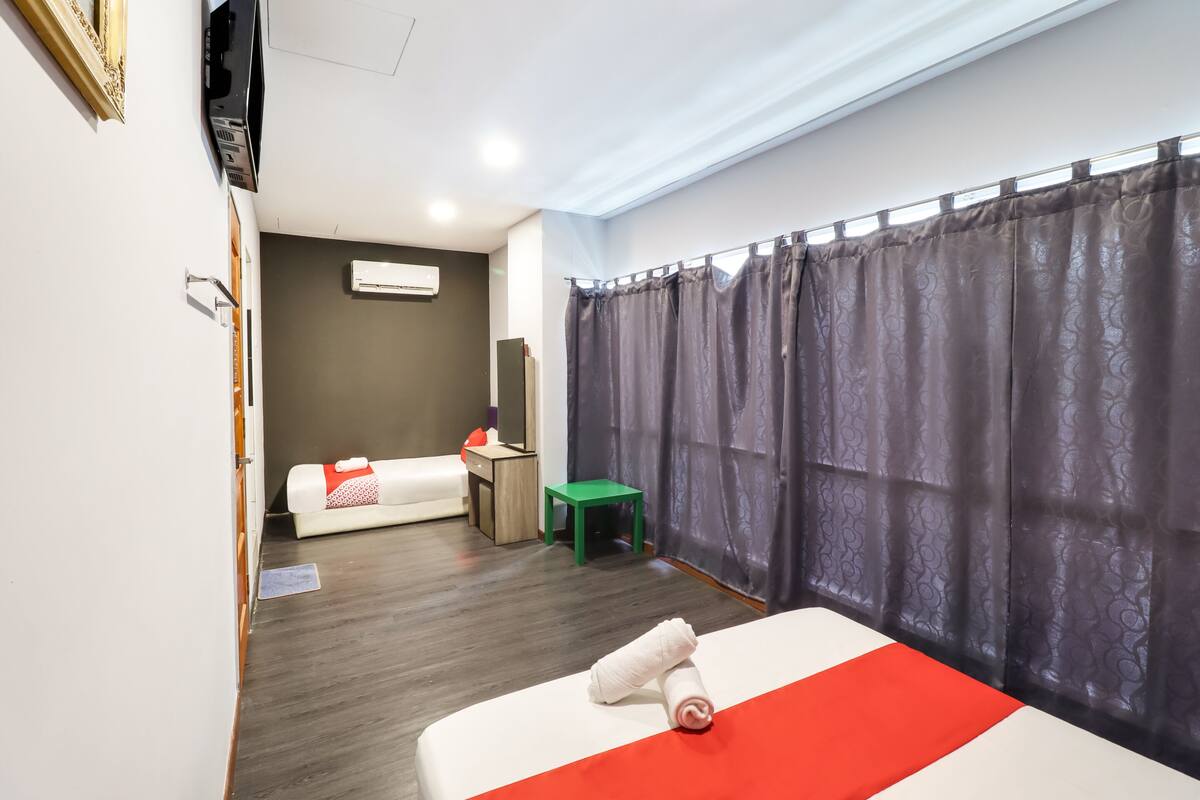 Een hotelkamer met een bed, een tafeltje, een groene kruk, een bank en een gordijn.