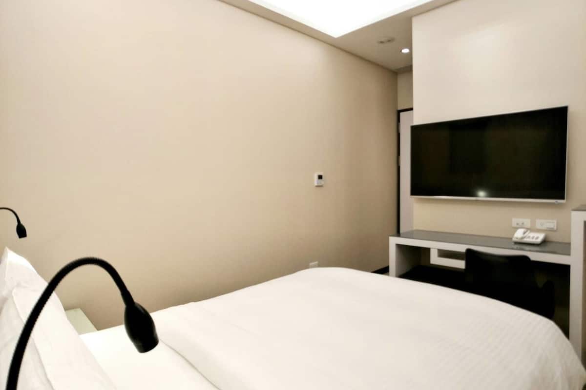 A hotel room with a bed, a desk with a flat-screen TV, and a ceiling light.