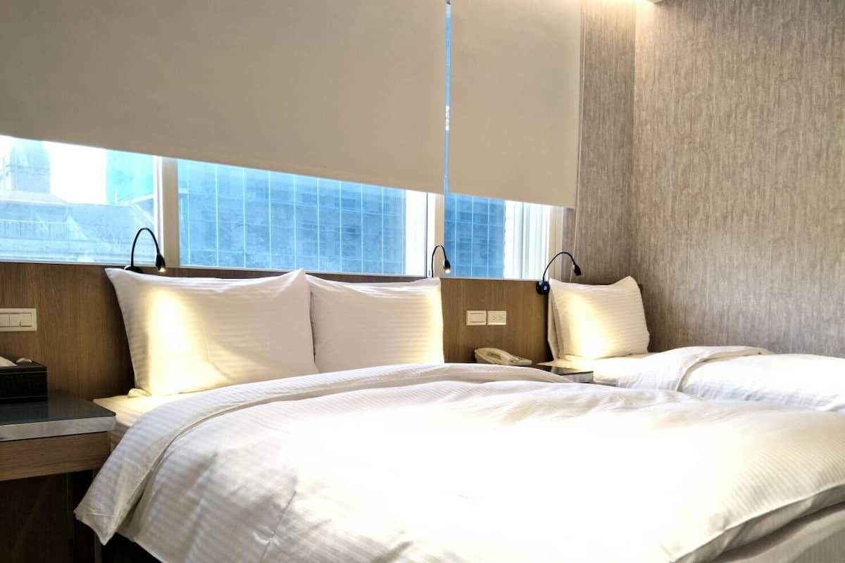 A hotel room with a large bed, bedside tables, a window with blinds, and a telephone on the nightstand.