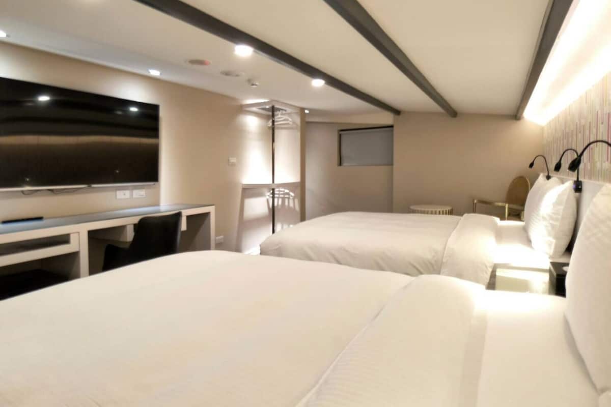 A hotel room with two beds, a desk, a TV, and a window.