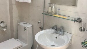 Un baño con inodoro, lavamanos, repisas de vidrio con artículos de aseo y espejo.
