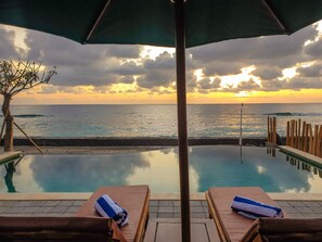 A poolside view with two lounge chairs and a large umbrella, overlooking the ocean at sunset. - Juan Beach Bungalow (Penida Island)
