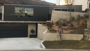 A modern two-story house with a garage, a landscaped garden, and a view of a hilly landscape.
