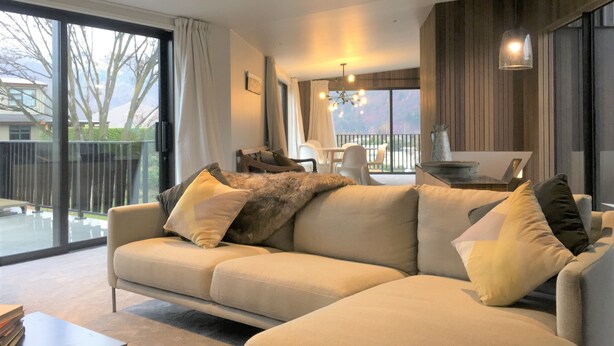A modern living room with a beige sectional sofa, a dining area with a table and chairs, and a large sliding glass door leading to a balcony.