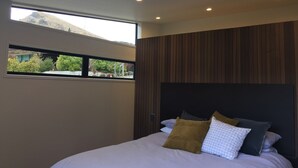 A modern bedroom with a large bed, a wooden headboard, and a window overlooking a mountain and greenery.