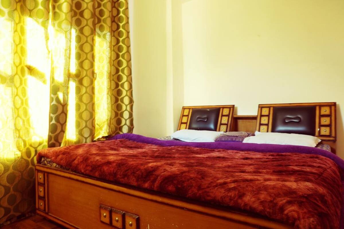 Une chambre à coucher avec un lit en bois, des rideaux à motifs et une tête de lit agrémentée d’un miroir.