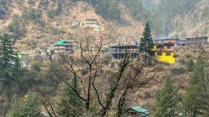 A mountainous area with several buildings, including a prominent yellow structure and a traditional building on a hill. - Nomads Hostel (Bhuntar)