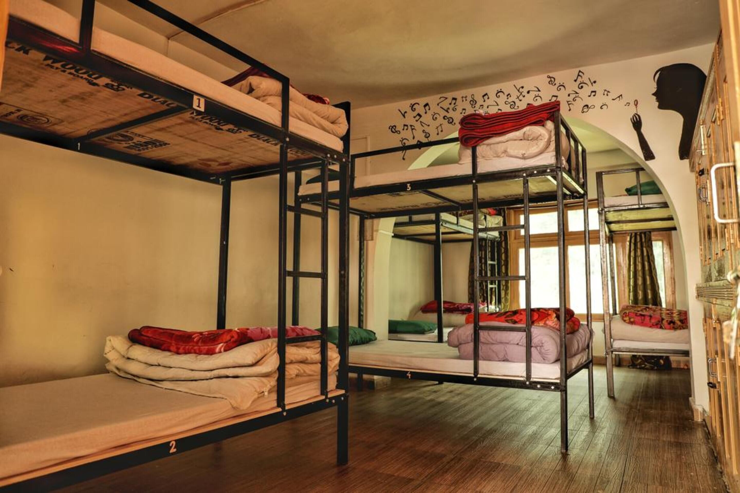 Un dormitorio con literas, camas numeradas y un mural en la pared.