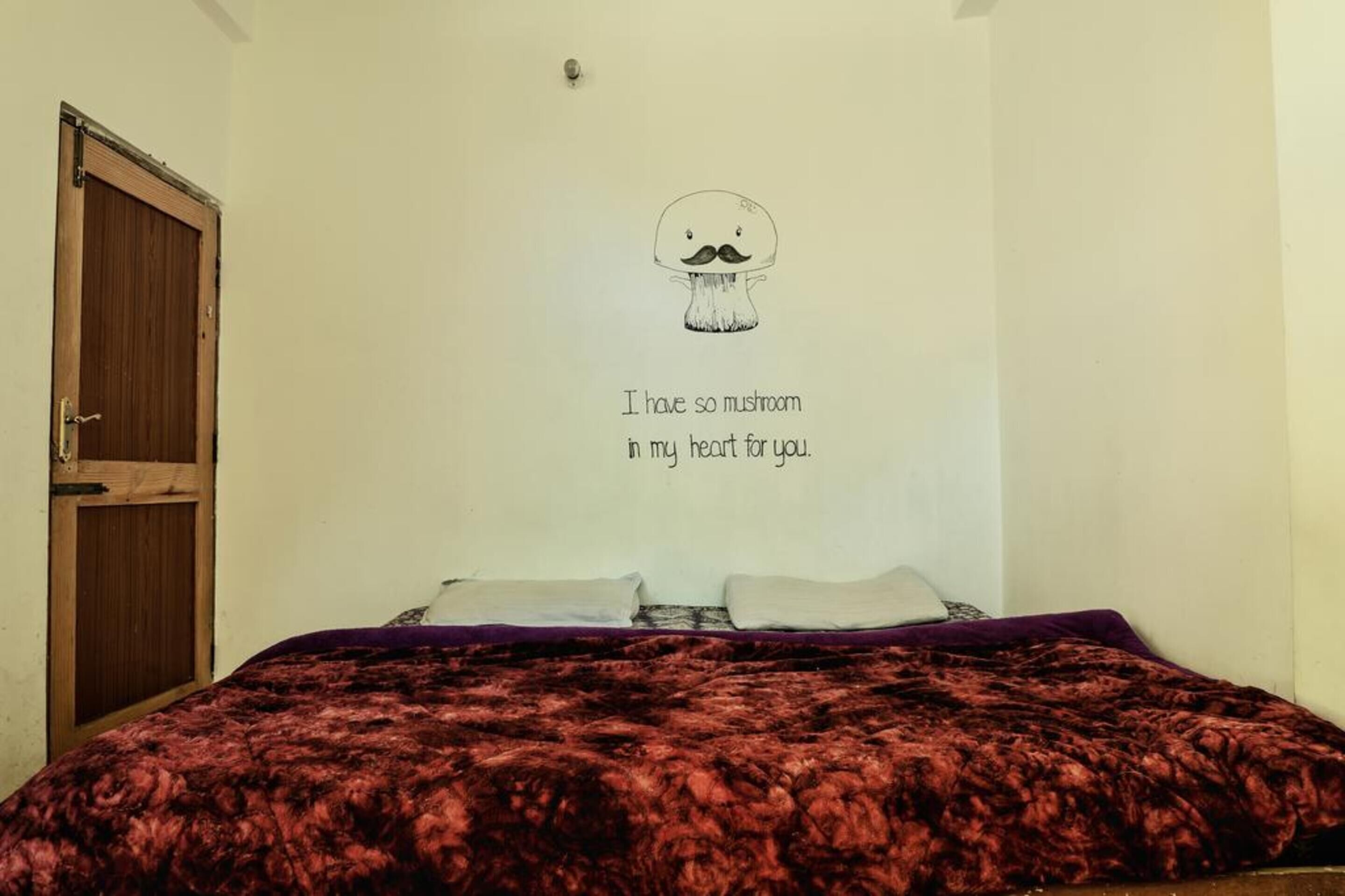 A bedroom with a bed, a wooden door, and a wall with a drawing of a mushroom and text.