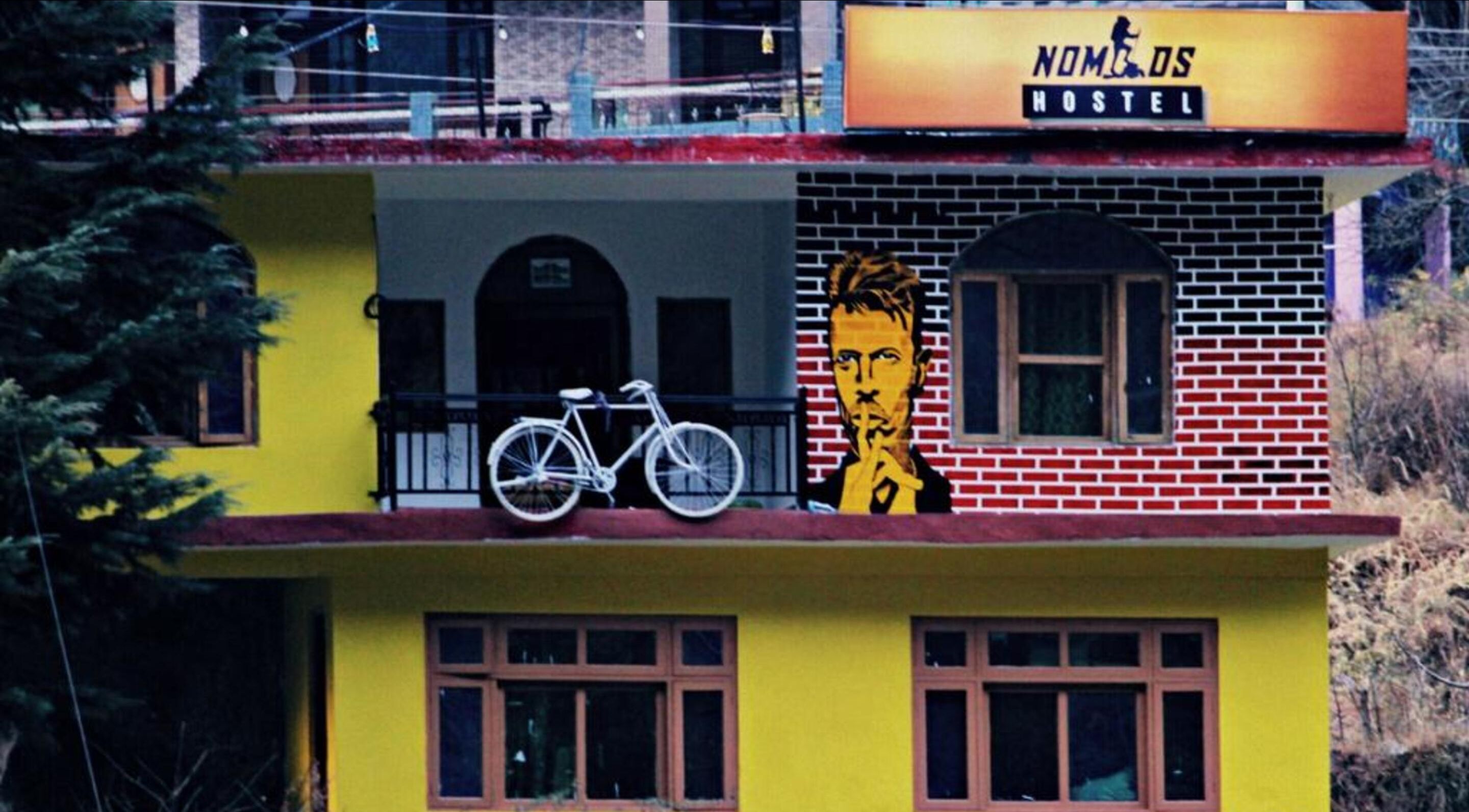 Un hostal con fachada amarilla, una bicicleta estacionada en el balcón y un mural con el rostro de un hombre.