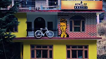 Un hostal con fachada amarilla, una bicicleta estacionada en el balcón y un mural con el rostro de un hombre.
