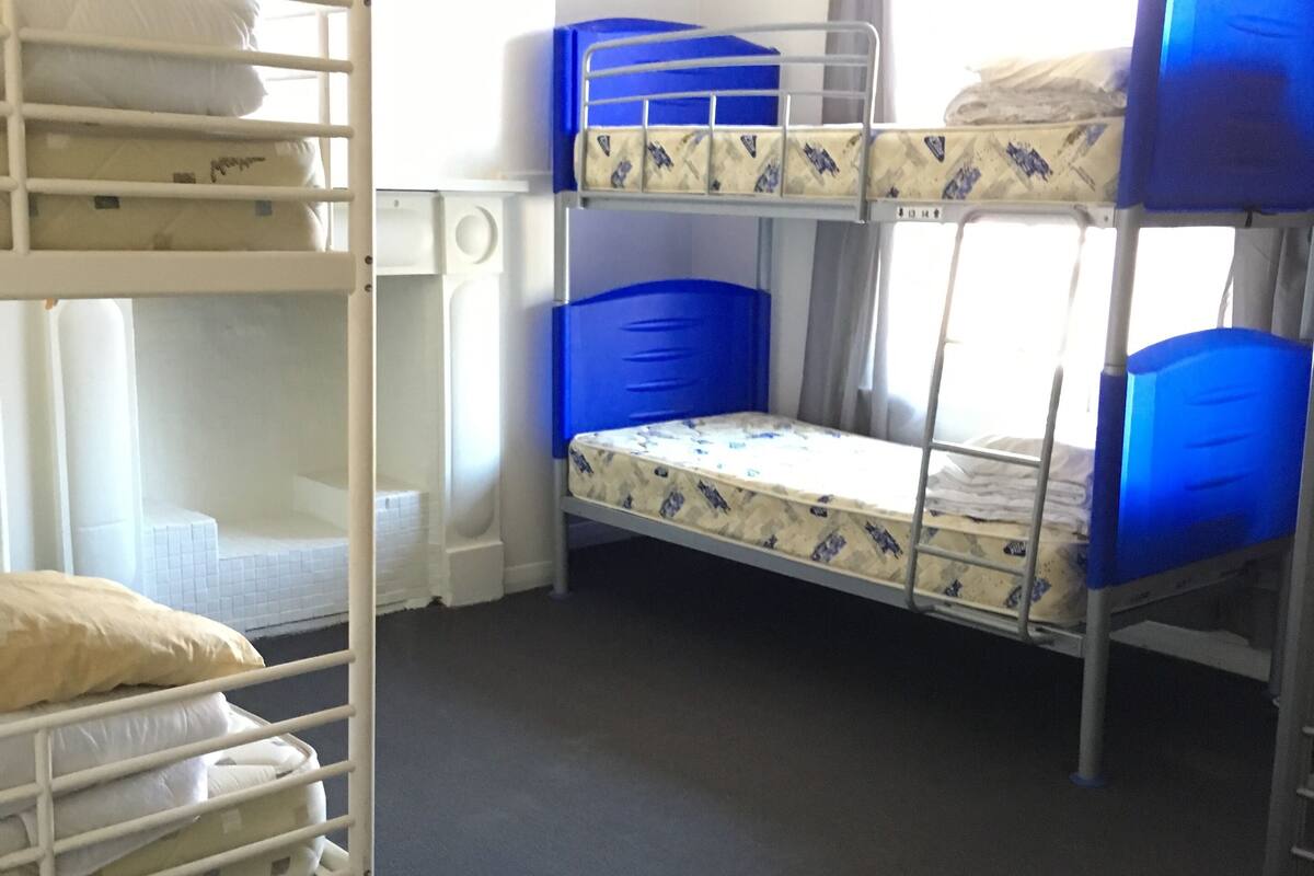 A dormitory room with bunk beds, a radiator, and a window with curtains.
