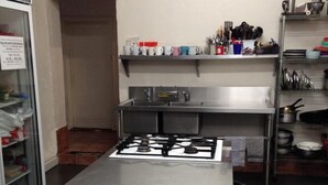 A kitchen with a stainless steel stove, shelves with kitchenware, and a refrigerator. - Shingos Backpackers (Adelaide)