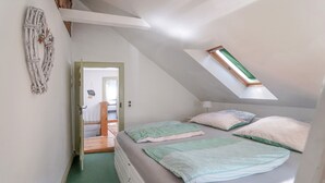 A bedroom with a sloped ceiling, a skylight, a bed with multiple pillows, and a wall-mounted decoration.